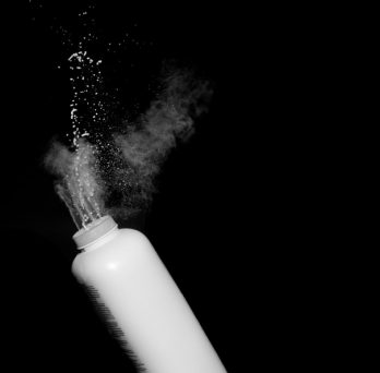 White powder flies into the air from a squeezed bottle of talcum powder.
                  