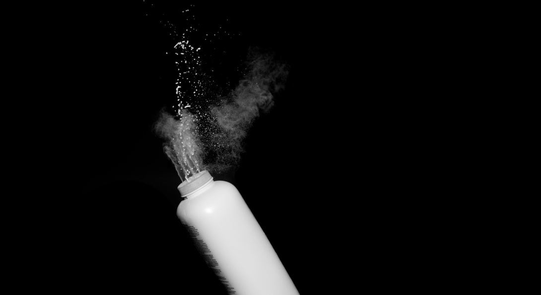 White powder flies into the air from a squeezed bottle of talcum powder.