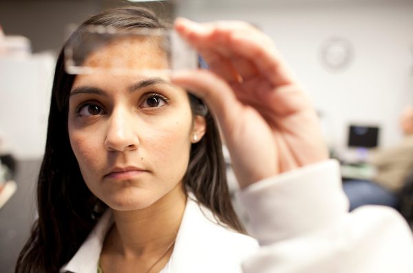 A medical professional examines a glass slide with a substance on it.
