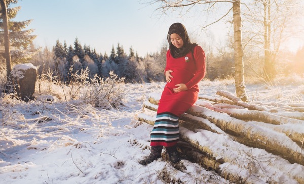 A pregnant woman stands outside while posing for a photo in a winter scene.